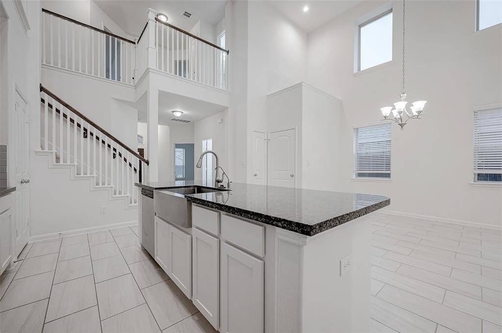 This modern home features an open-concept design with high ceilings, a sleek kitchen island with a dark countertop, and ample natural light from large windows. The staircase leads to a second level, adding to the spacious feel.