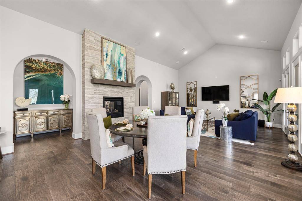 This spacious living area features elegant hardwood floors, a modern fireplace, and high ceilings. The room is tastefully decorated with contemporary furnishings, a dining space, and ample natural light from large windows.