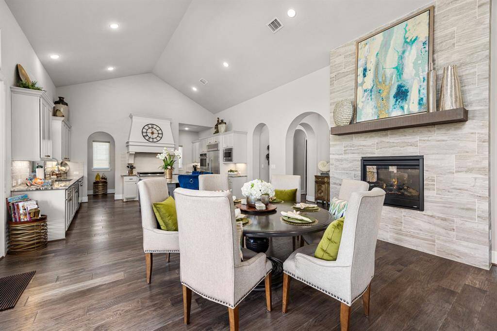 This inviting open-concept living space features a modern kitchen with white cabinetry and a spacious dining area. The room is highlighted by a cozy fireplace and stylish decor, creating a warm and contemporary atmosphere perfect for gatherings.