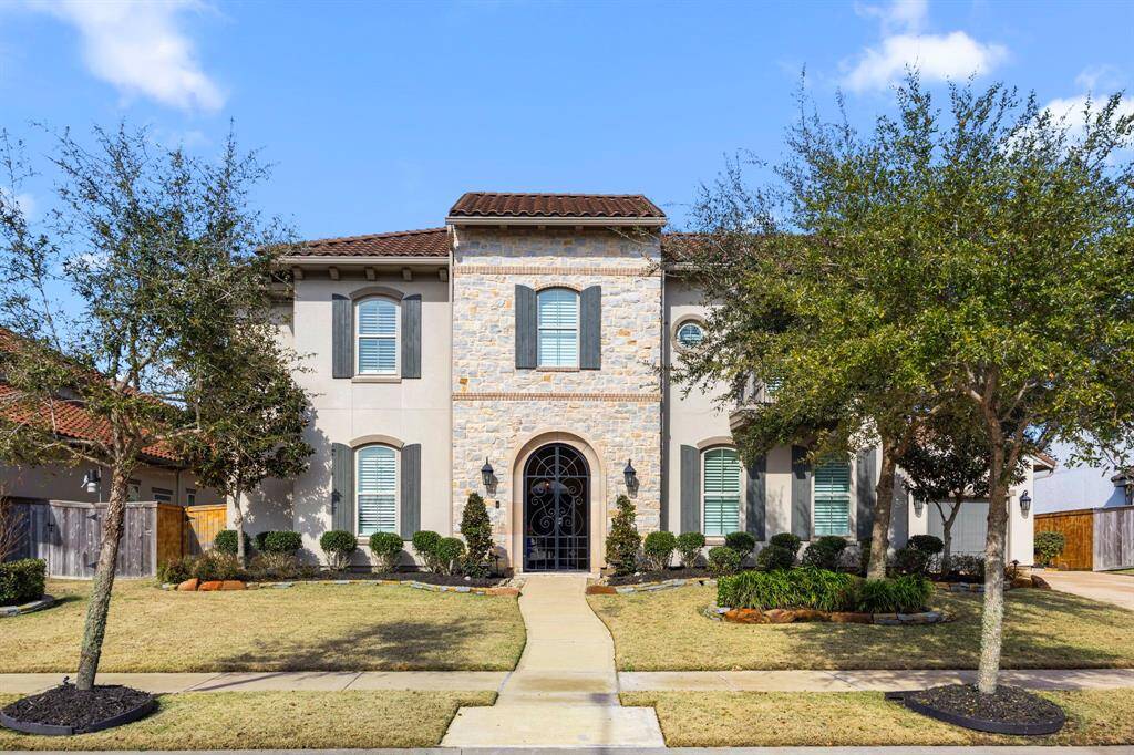 This beautiful two-story home features a classic facade with stone accents, a tile roof, and charming shutters. It is surrounded by well-manicured landscaping and trees, providing excellent curb appeal, only steps to the lake.