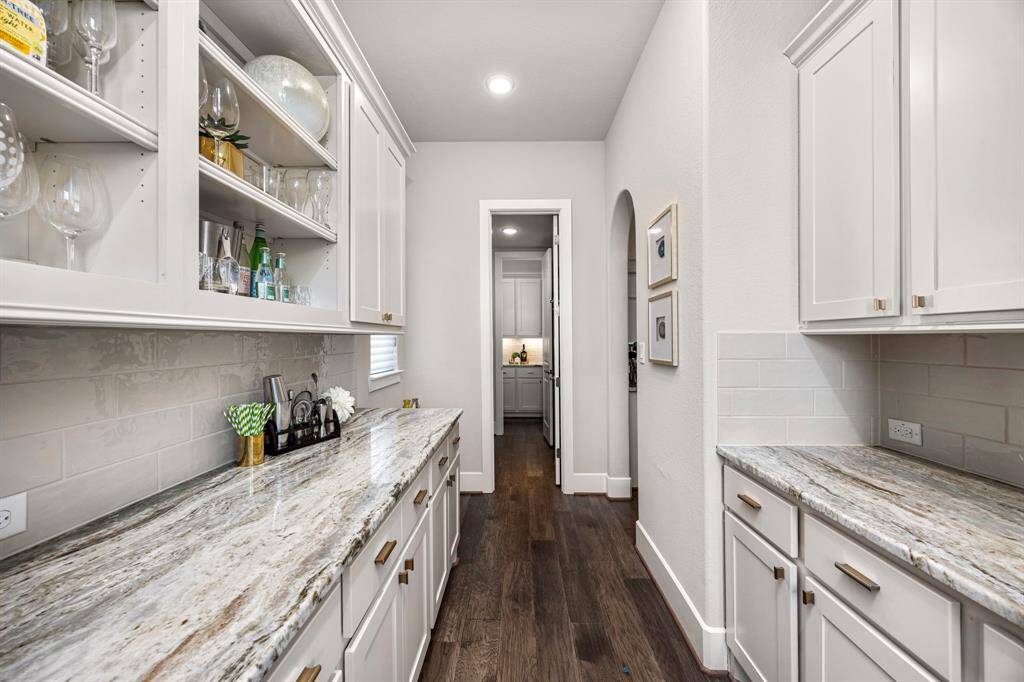 This photo showcases a stylish butler's pantry with elegant granite countertops, ample cabinet storage, and open shelving. The space features hardwood floors, soft neutral tones, and recessed lighting, offering a seamless transition to the main kitchen area.