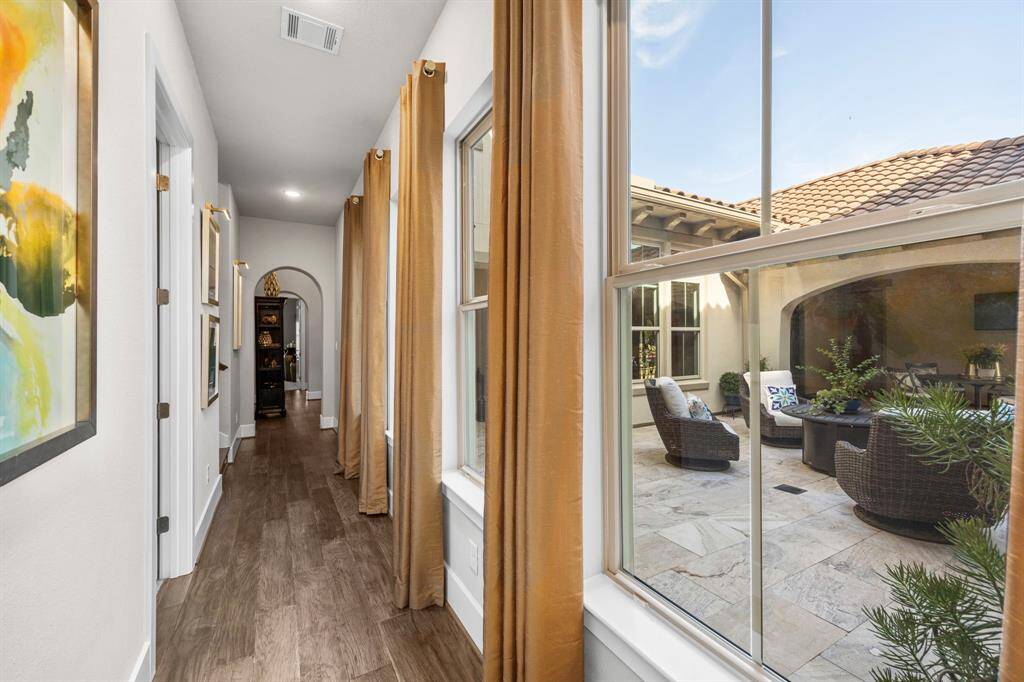 This photo features a bright, inviting hallway with wood flooring and large windows offering a view of a cozy, courtyard. The hallway leads to two secondary bedrooms downstairs each with their own private bath.
