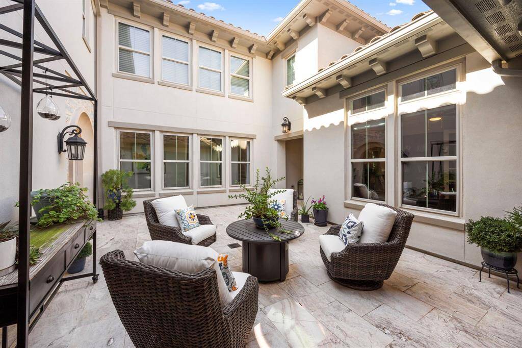 Charming courtyard with comfortable wicker seating and lush potted plants, surrounded by large windows for natural light. Perfect for outdoor relaxation and entertaining.