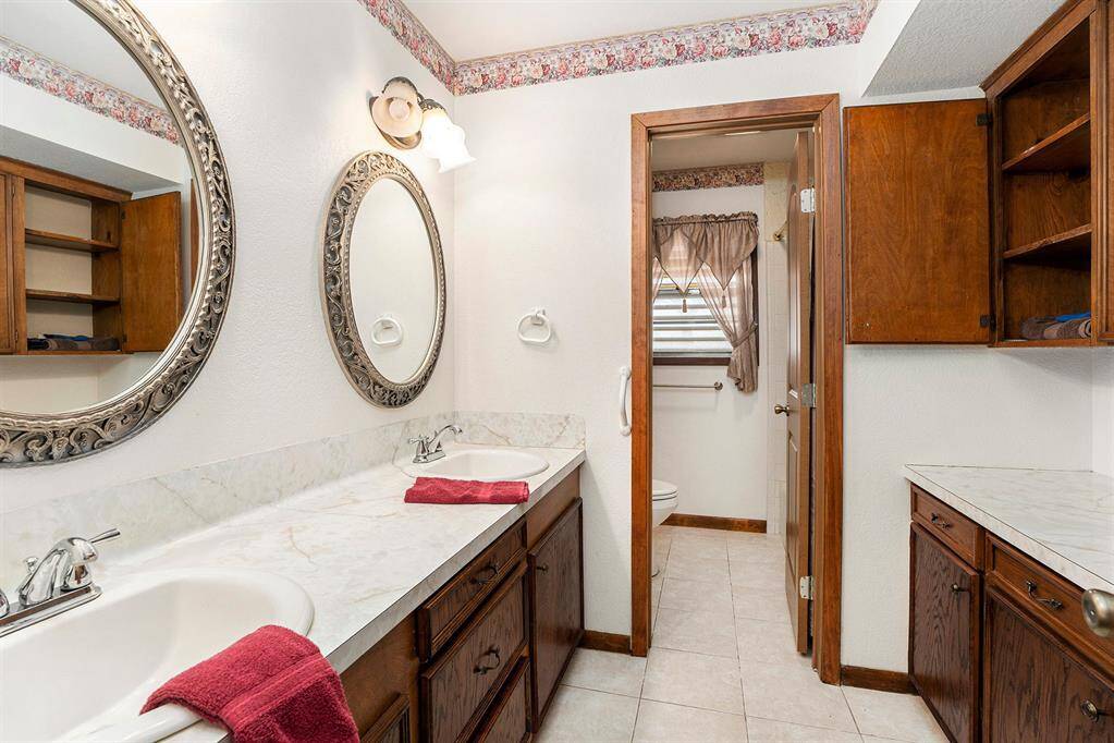 Spacious hall bath featuring dual sinks, ample storage, and elegant solid wood cabinets throughout.