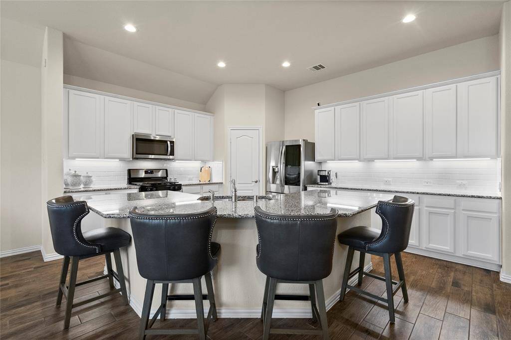 This modern kitchen features sleek white cabinetry, stainless steel appliances, and a spacious granite countertop island with seating for four to six.