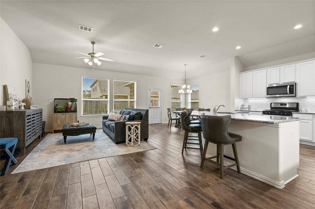 This open-concept living space features a modern kitchen with stainless steel appliances and a breakfast bar, seamlessly flowing into a cozy living area with wood flooring. Large windows provide ample natural light, and a dining area is situated nearby, perfect for entertaining.