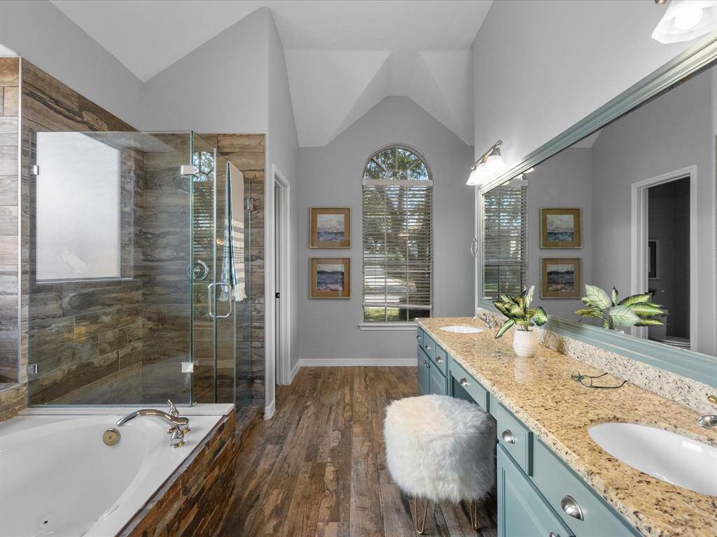 Luxurious bathroom with stone accents, a soaking tub, and a glass-enclosed shower. Elegant double vanity with granite countertops and a charming vanity seating area for convenience.