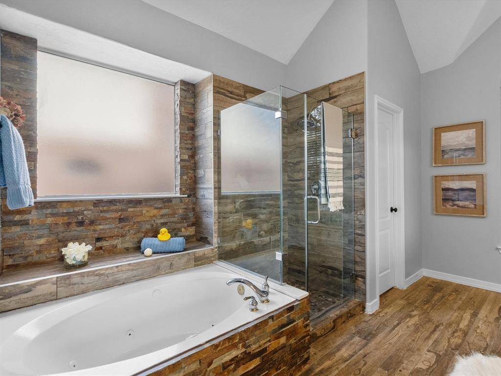 Relax in the spa-like bathroom featuring a jetted tub, stone accents, and a frameless glass shower