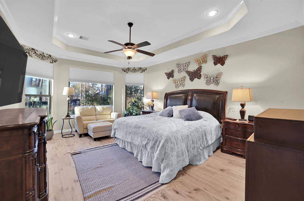 The primary retreat features a tray ceiling with three windows, offering an excellent view of the surrounding landscape. Natural light floods the room, creating a warm, inviting atmosphere. The sleek design works perfectly with a neutral color backdrop. The connection between indoor and outdoor living feels seamless, enhancing the serene and peaceful ambiance of the retreat.