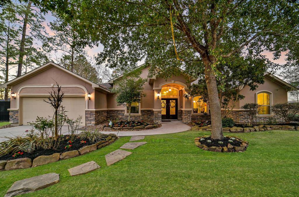 This stunning home sits majestically surrounded by meticulous landscaping. The elegant exterior of the house features a combination of classic stone and stucco, with large windows and stately double doors.