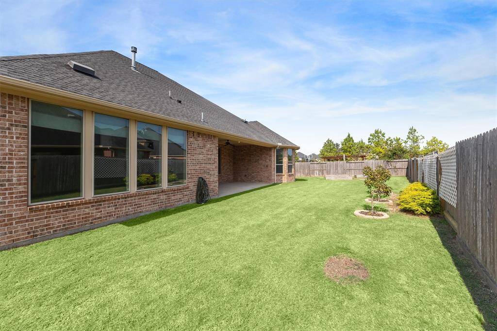 This is a well-maintained backyard with a manicured lawn and privacy fencing, part of a single-story brick home featuring large windows and a covered patio area.