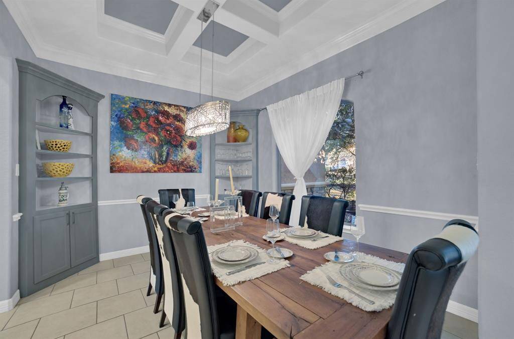 The formal dining room exudes elegance and sophistication with a beautiful, coffered ceiling, built in shelves and a large window overlooking the serene front yard. The room is accented by a tasteful chandelier.