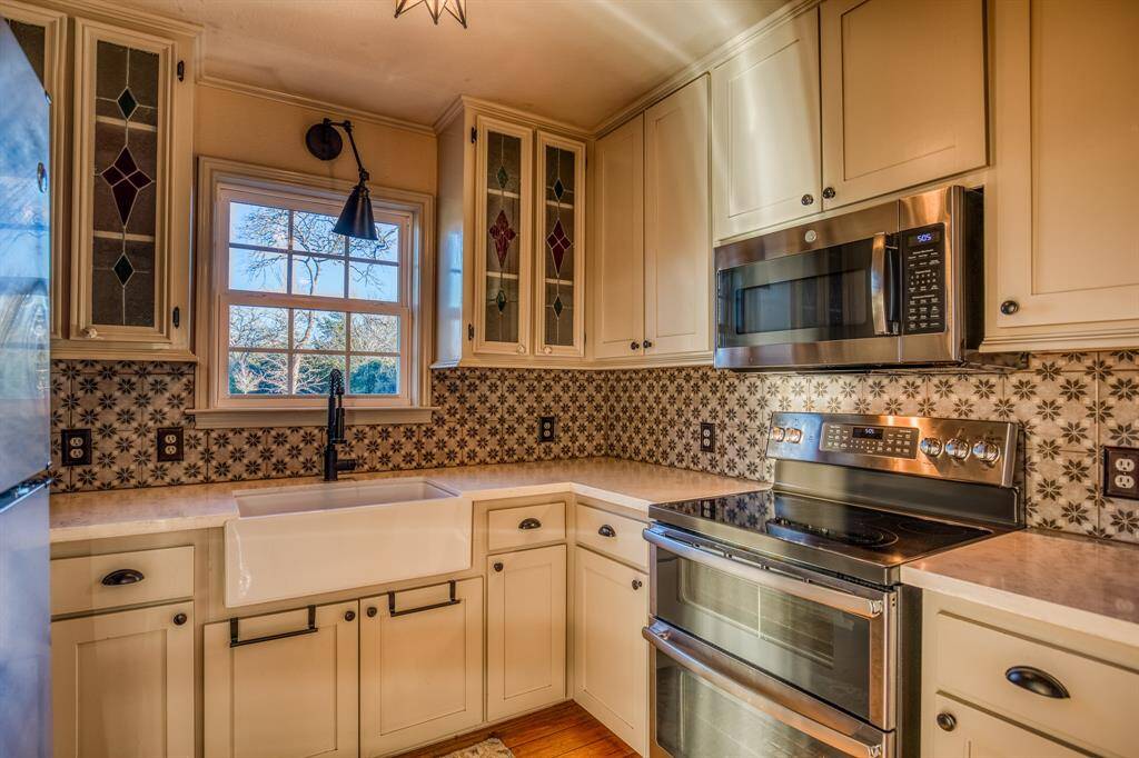 This farmhouse kitchen offers the perfect combination of hard wood flooring, classic quartz countertops with soft color tones, double ovens, a built-in microwave, dishwasher, a gorgeous farmhouse sink, stained glass windows in the cabinets, detailed backsplash with the perfect lighting & amazing views of the wild deer roaming through the front yard. Don't miss out on this charming space.