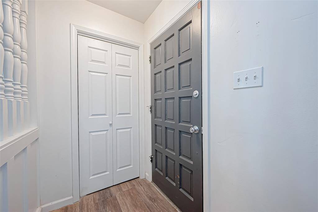 This entryway features a stylish dark gray front door with a geometric panel design, adjacent to a white double closet. The space is accented by light wood flooring and a clean, white wall with a switch panel.