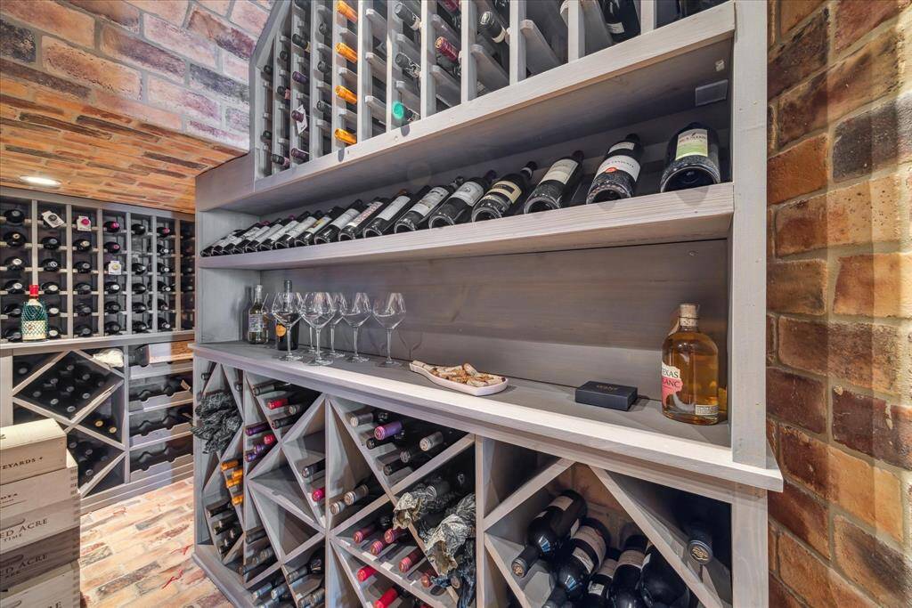 Climate controlled wine room with plenty of storage, brick walls and floors, slanted bottle display and corking station.