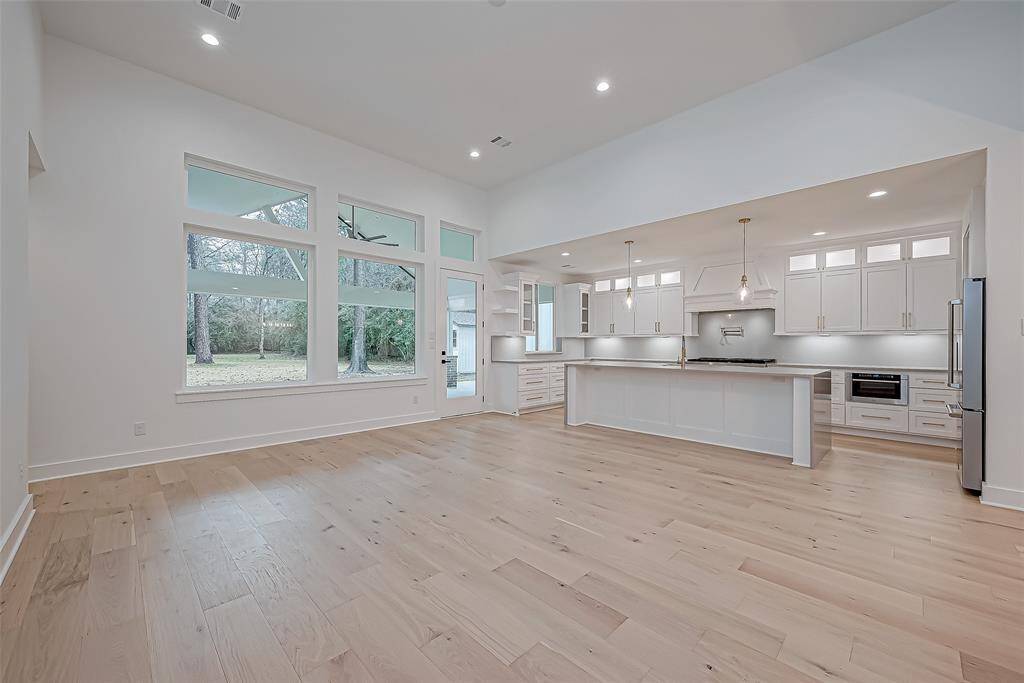 Spacious, open-plan living area with  wood flooring and abundant natural light from large windows overlooking a wooded backyard.