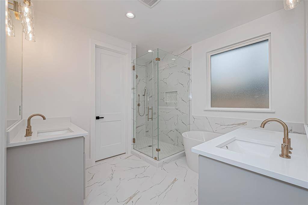 Dual sinks with sleek fixtures, a frameless glass shower, and a freestanding tub. The space is bright, with white marble-style tiles and a frosted window for privacy.