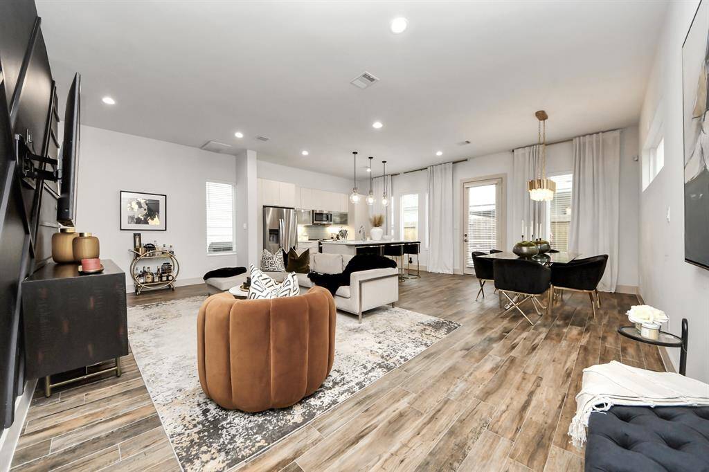 This open-concept living area features modern decor with a cozy seating arrangement, sleek hardwood floors, and abundant natural light. The kitchen is equipped with stainless steel appliances and a stylish dining area. Ideal for entertaining and comfortable living.