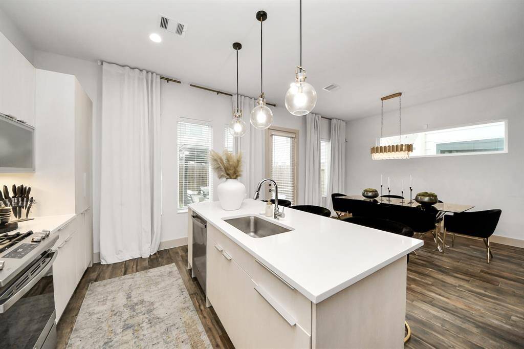 This photo showcases a modern, open-concept kitchen and dining area. The kitchen features sleek cabinetry, a central island with a sink, and contemporary lighting fixtures. The adjacent dining space includes a stylish table with elegant chairs, all set on warm wood flooring, creating a cozy and inviting atmosphere.