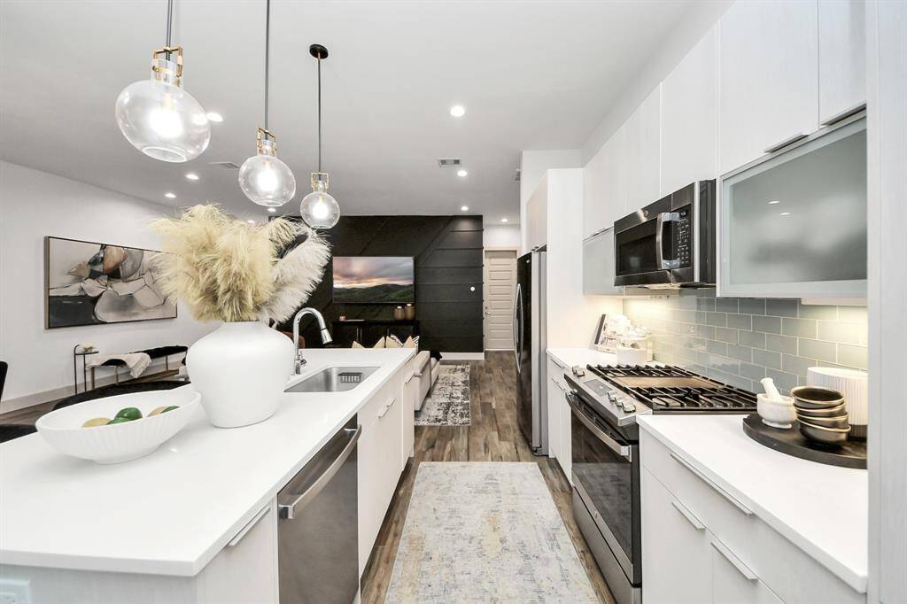 Modern kitchen with sleek white cabinetry, stainless steel appliances, and a stylish backsplash. The open layout flows into a cozy living area, featuring contemporary lighting and elegant decor. Perfect for entertaining and everyday living.