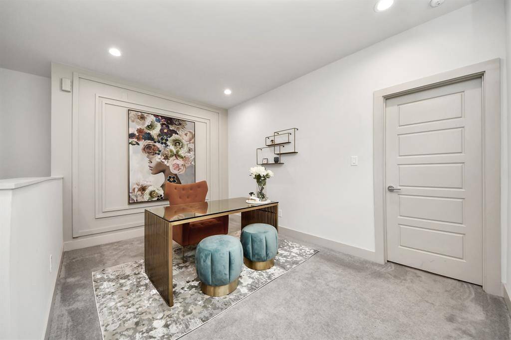 This photo showcases a stylish, modern home office with a sleek desk, plush seating, and elegant decor. The space is well-lit with recessed lighting and features a large, artistic wall piece, creating a sophisticated and inviting work environment.