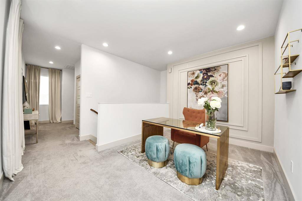 This photo showcases a stylishly decorated hallway with a modern desk and seating area. The space features soft carpeting, recessed lighting, and tasteful wall art, creating a cozy and inviting atmosphere.