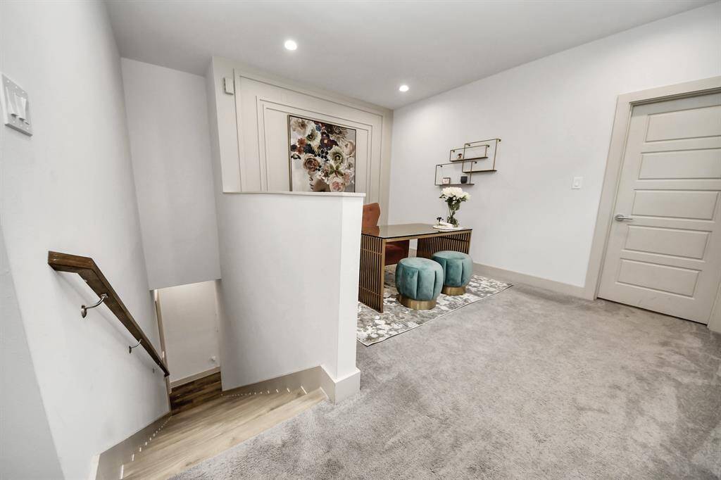 This photo showcases a cozy, well-lit landing area with a modern desk setup, featuring two teal stools and a decorative floral artwork. The space is carpeted and leads to a staircase with wooden handrails, suggesting a functional yet stylish home environment.