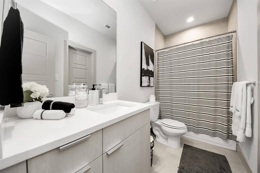 This modern bathroom features a sleek vanity with ample storage, a spacious mirror, and contemporary fixtures. The shower area includes a striped curtain, adding a stylish touch. Neutral tones create a clean and inviting atmosphere.