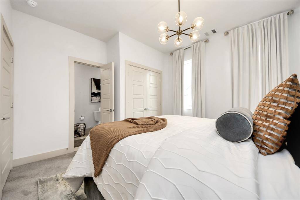 This bedroom features a modern design with neutral tones, a stylish chandelier, and ample natural light. It includes an en-suite bathroom and spacious closet, ideal for comfortable living.