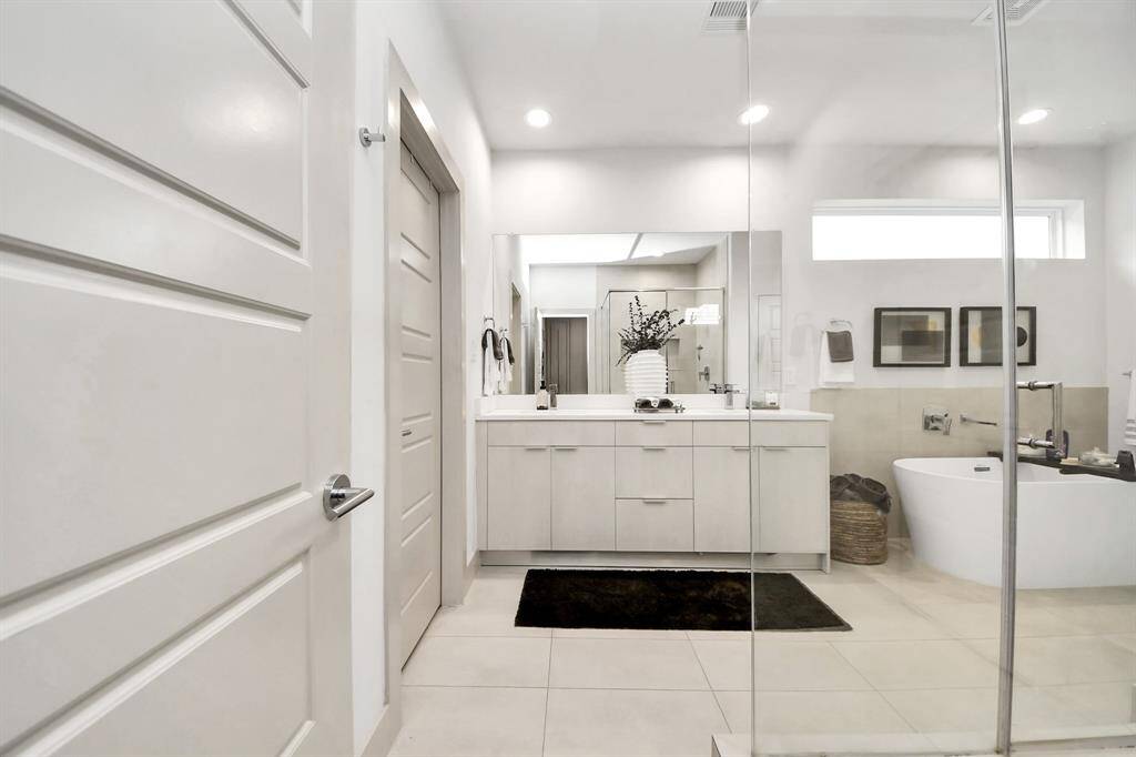 This modern bathroom features a sleek design with light cabinetry, a large mirror, and a spacious walk-in shower. It includes a luxurious freestanding bathtub and elegant tile flooring, providing a clean and contemporary feel.
