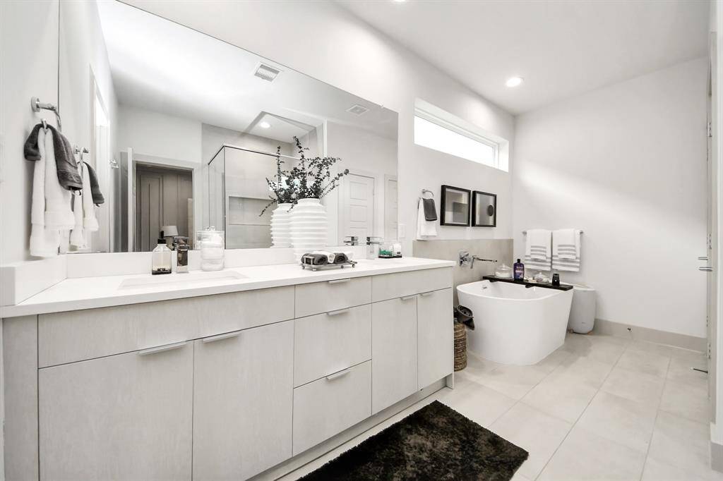 This modern bathroom features a sleek, spacious design with a large vanity, elegant fixtures, and a freestanding tub. The neutral color palette and ample natural light create a serene atmosphere. The glass-enclosed shower and stylish decor add a touch of luxury.