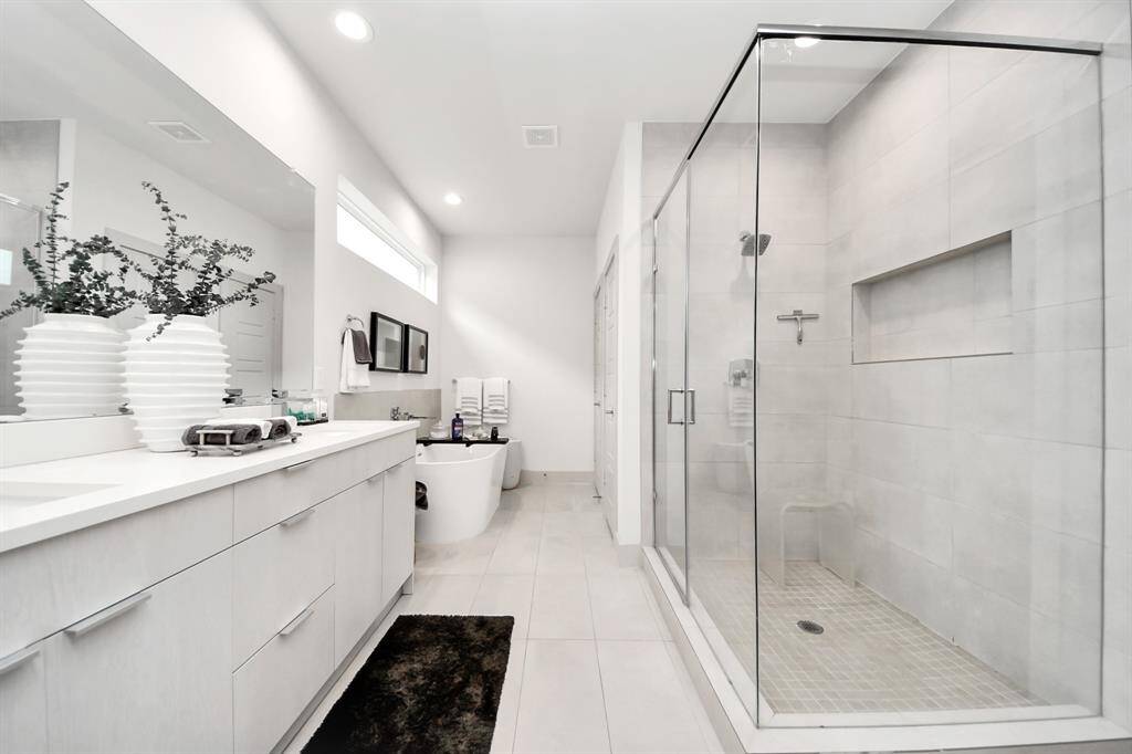 This modern bathroom features a spacious glass-enclosed shower, a freestanding bathtub, and a long double-sink vanity. The neutral color palette and sleek design create a bright and airy atmosphere.