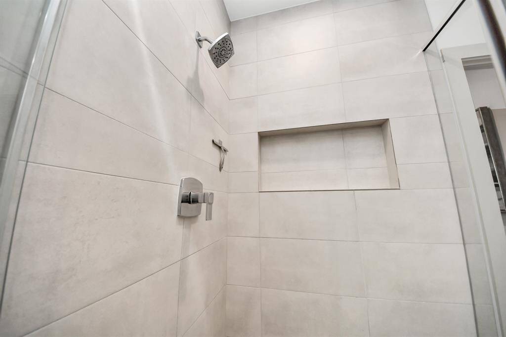This photo showcases a modern shower with sleek, large beige tiles. It features a built-in niche for storage and a contemporary showerhead, offering a clean and minimalist design.