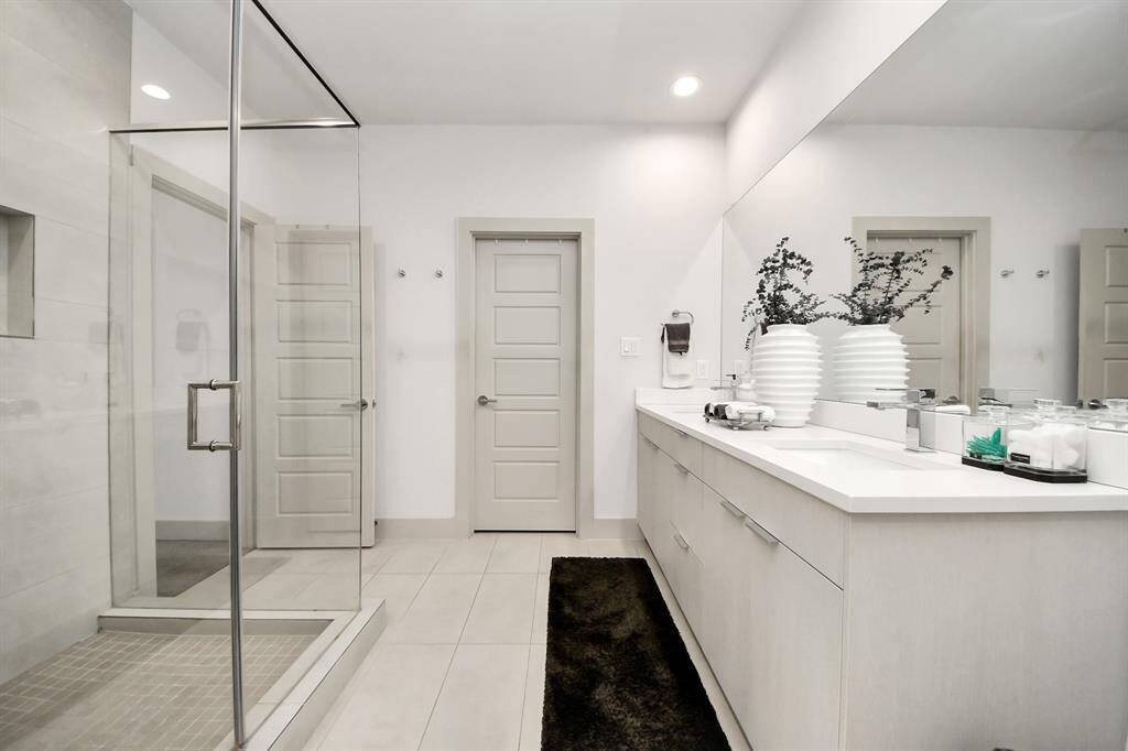 This bathroom features a modern design with a spacious glass-enclosed shower, sleek dual-sink vanity, and neutral tones. The room is bright with ample space for storage and stylish accents.