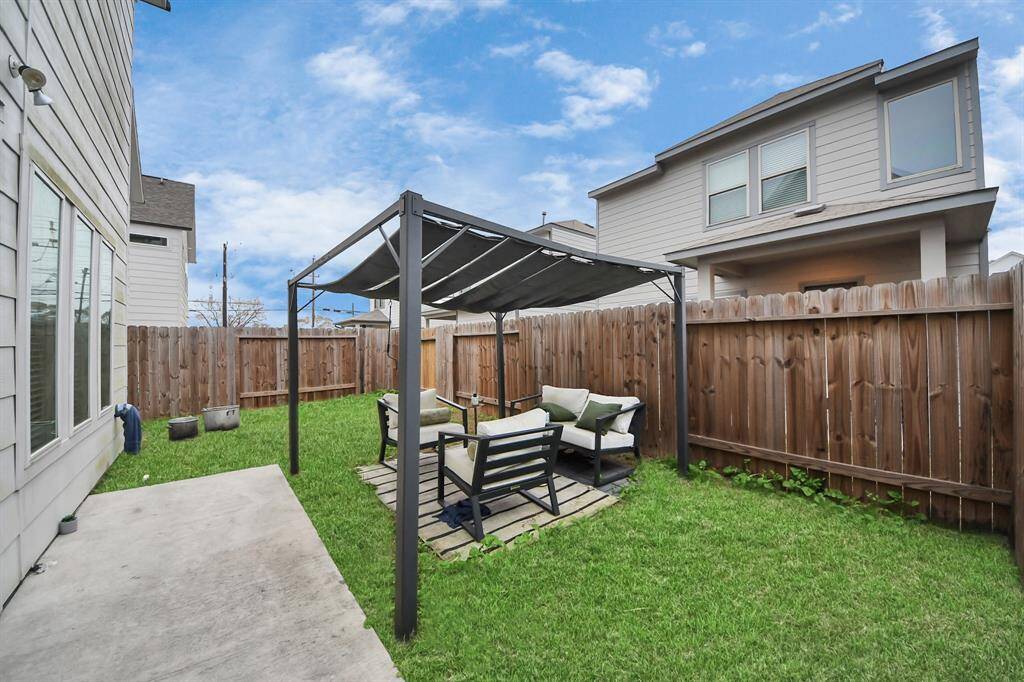 Charming backyard with a covered seating area on a small patio, surrounded by a wooden fence. Ideal for outdoor relaxation and entertaining.