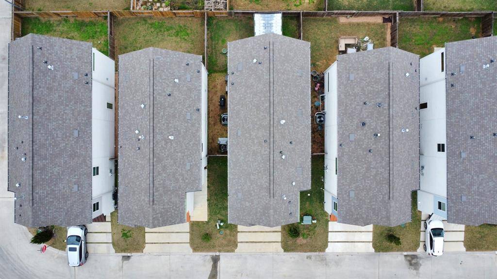 This aerial photo shows a row of modern townhouses with identical roof designs and small fenced backyards. The houses are closely spaced, with driveways leading to each unit. The layout is efficient, ideal for a suburban community.