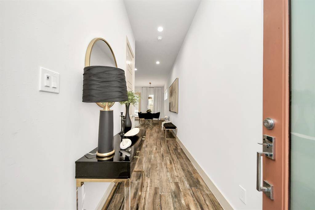 This is a modern, well-lit hallway with wood-style flooring. It features a sleek console table with decorative items and a stylish lamp. The space leads into a living area, offering a sense of openness and elegance.