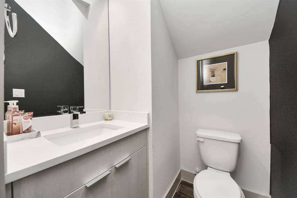 This photo shows a modern, compact bathroom with a sleek white vanity, dark accent wall, and a toilet. The space is well-lit, featuring contemporary fixtures and a framed picture for decoration.