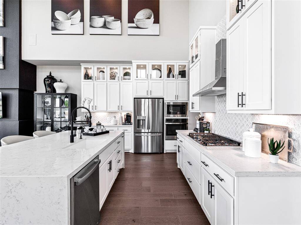 This kitchen features a modern design with white cabinetry, stainless steel appliances, and a spacious island with a built-in sink. The countertops are sleek and complemented by a stylish backsplash.