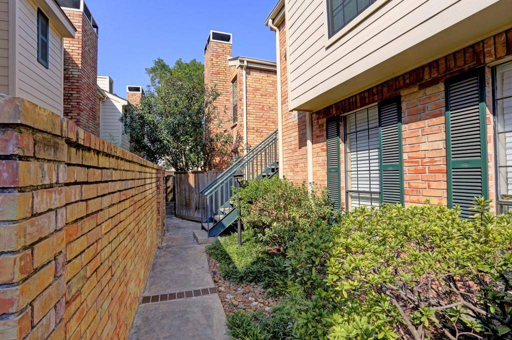 This condo features a charming brick townhouse/condo exterior with green shutters and well-maintained shrubs. A staircase leads to the front entrance, with parking at the backdoor, with two assigned parking spots.