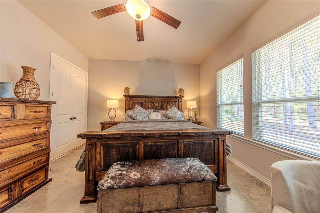 This cozy bedroom features rustic wooden furniture, including a large bed and a dresser. It has ample natural light from multiple windows and a ceiling fan for comfort.