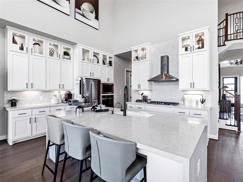 This modern kitchen features sleek white cabinetry with glass accents, a large island with seating, and a stylish range hood.