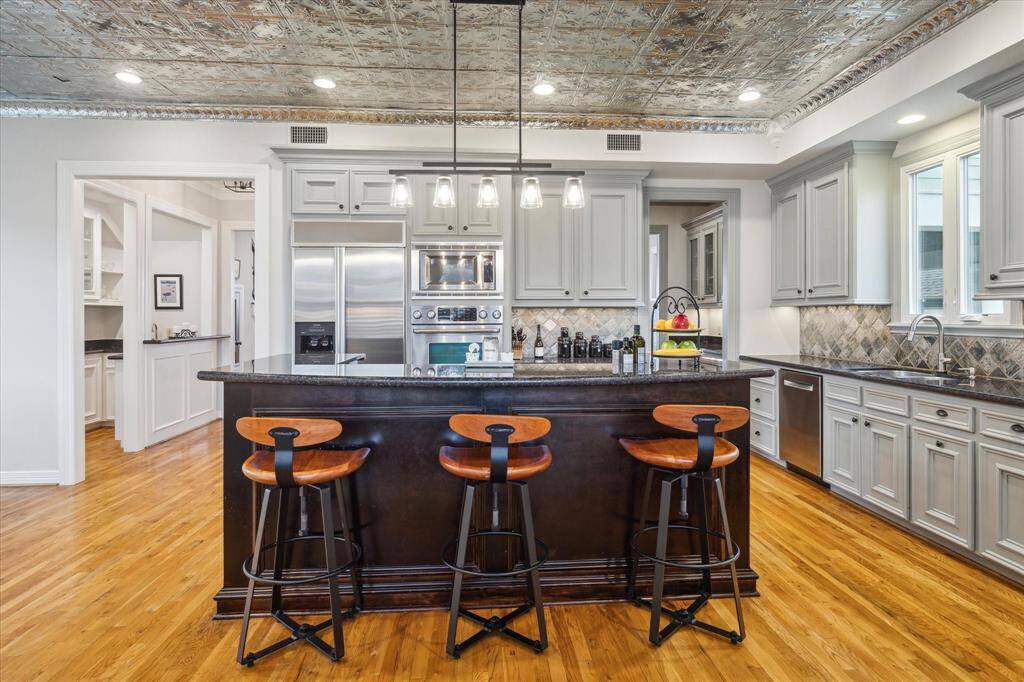 This stunning kitchen boasts a large breakfast bar highlighted by double ovens, sleek granite countertops, and a gorgeous tile backsplash that adds texture and style to the space.