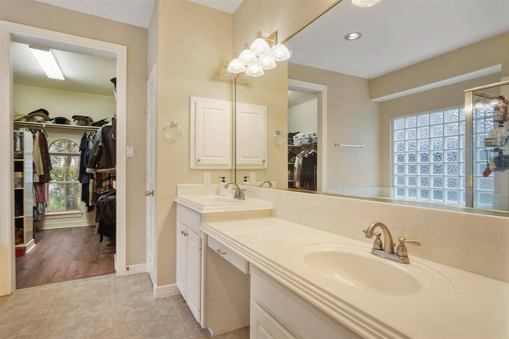 It is complete with tile floors, granite countertops, vanity area, double sinks, and a large mirror. The bathroom is open to the spacious walk-in closet which includes wood floors.