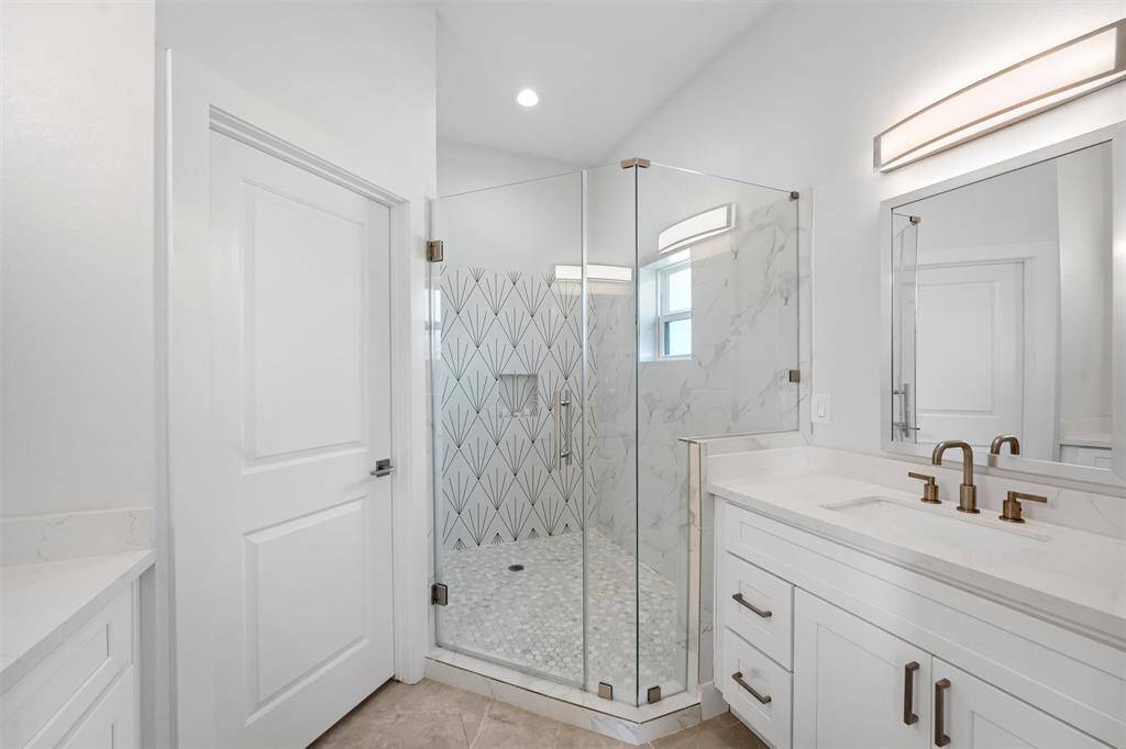 This stunning primary bath is designed for relaxation, featuring a spacious glass-enclosed shower with elegant tilework, dual vanities, and modern finishes.