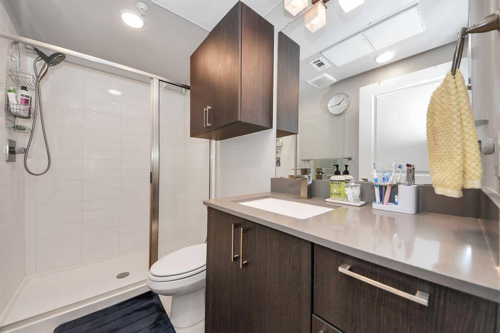 Modern bathroom with a sleek design, featuring a glass-enclosed shower, contemporary dark wood vanity with ample storage, and stylish fixtures. Well-lit with a neutral color palette.