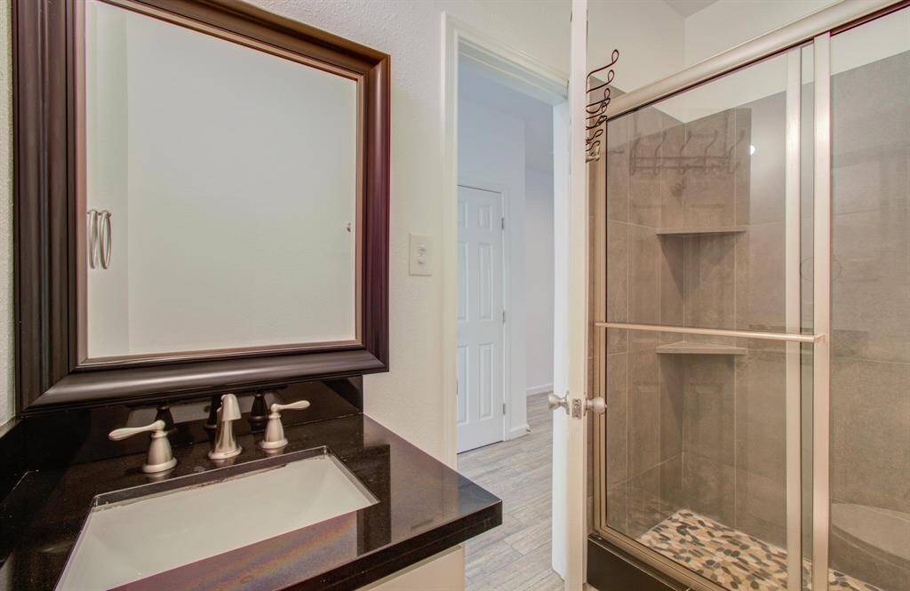 Another view of bathroom featuring countertop, framed mirror, glass-enclosed shower with tiled walls and built-in shelving, providing a sleek and functional space.