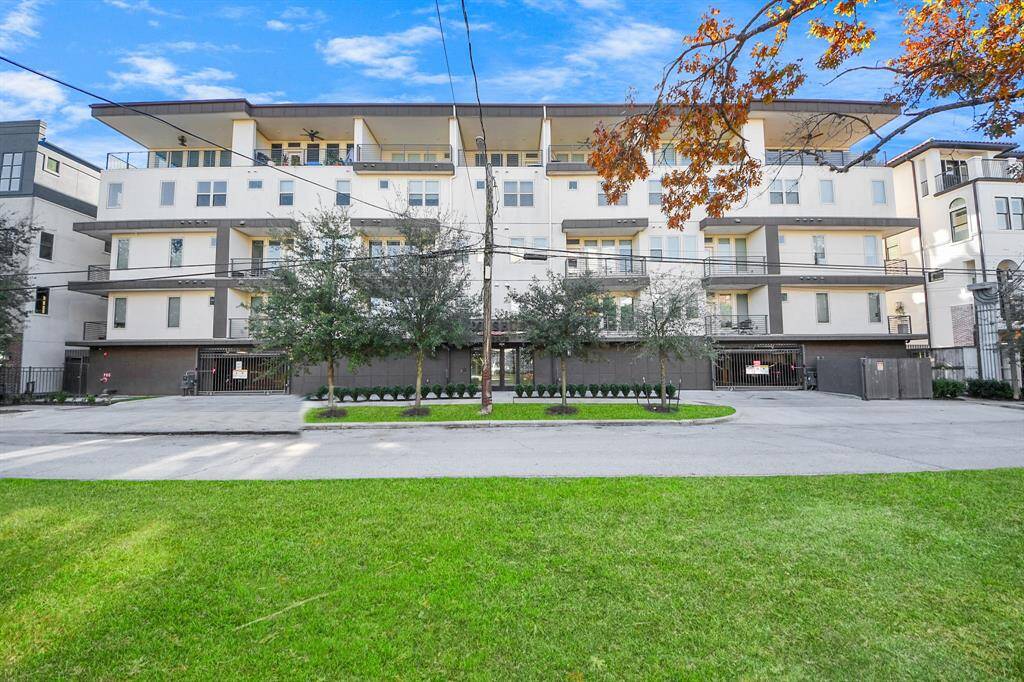 Modern building with a clean, white façade and several balconies. The property is surrounded by well-maintained greenery and trees, providing a pleasant curb appeal.