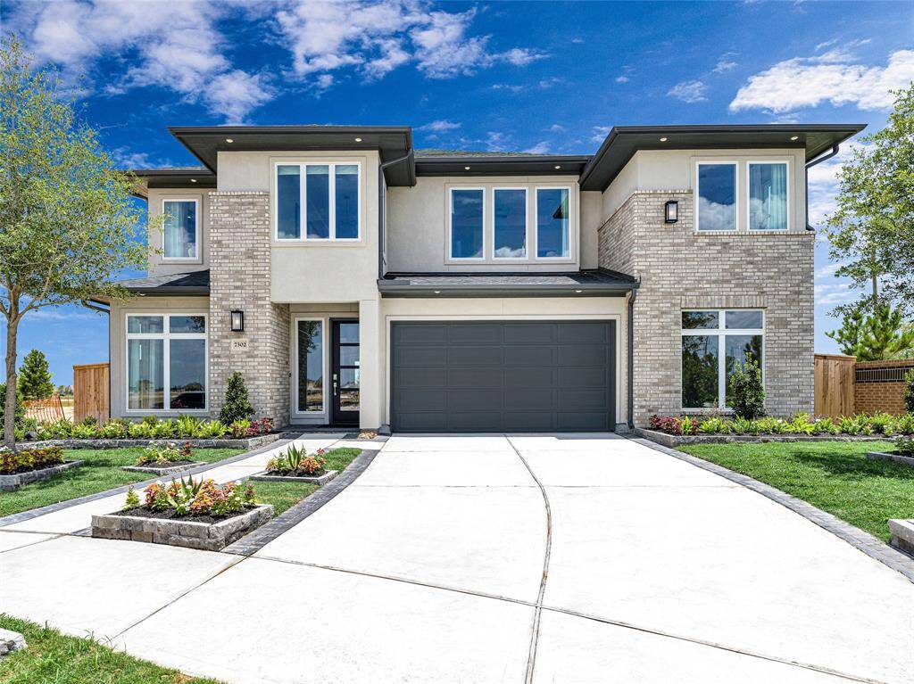 Modern two-story home with a sleek design, featuring large windows and a mix of brick and stucco exterior.
