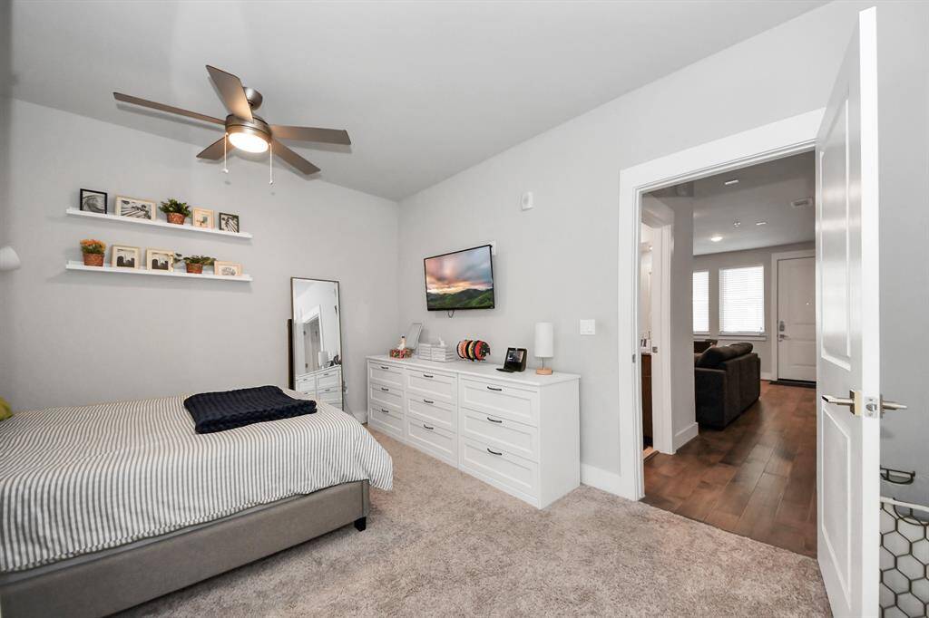 This bedroom features a modern design with neutral tones, carpeted flooring, and a ceiling fan.